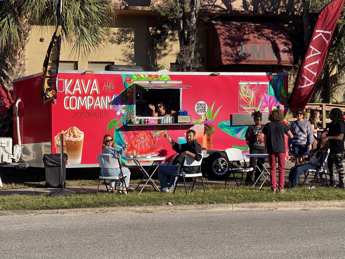 The pink Kava and Company bar trailer parked at an outdoor event with feather flags up and guests seated at the service window